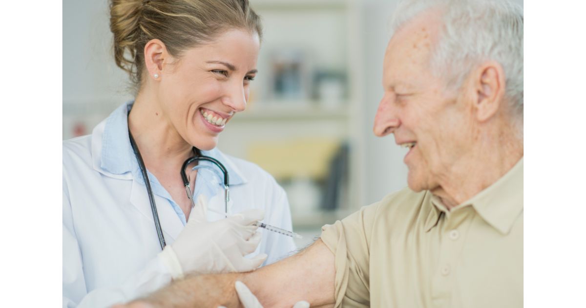 A healthcare professional smiling while administering a shot to an elderly patient, showing a caring and supportive interaction.