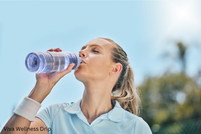 Active woman in a light blue shirt drinking water outdoors under a clear sky, emphasizing hydration and summer wellness.