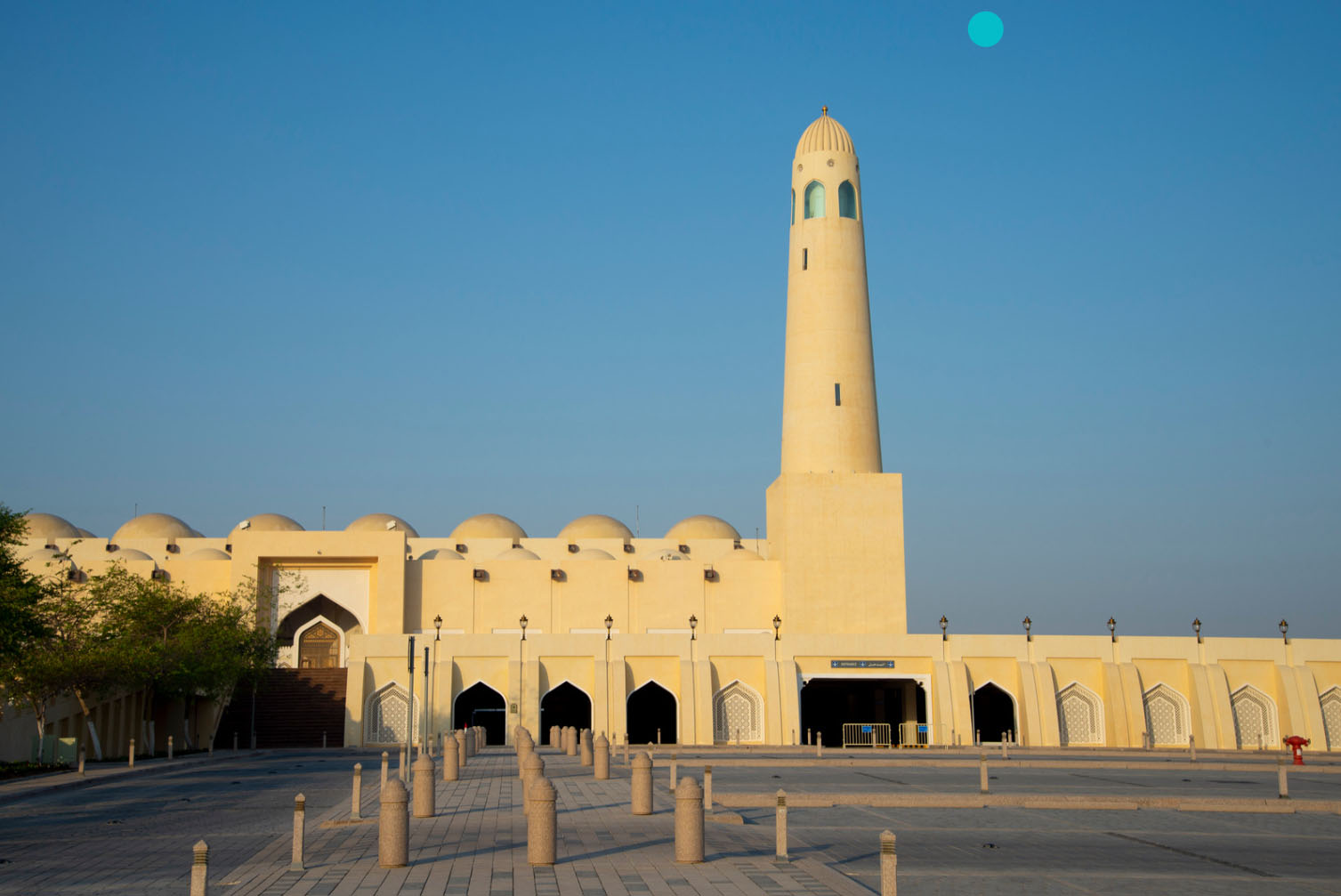 The Imam Muhammad ibn Abd al-Wahhab Mosque in Doha, Qatar, featuring traditional Islamic architecture with a tall minaret, domes, and a spacious courtyard under a clear blue sky.