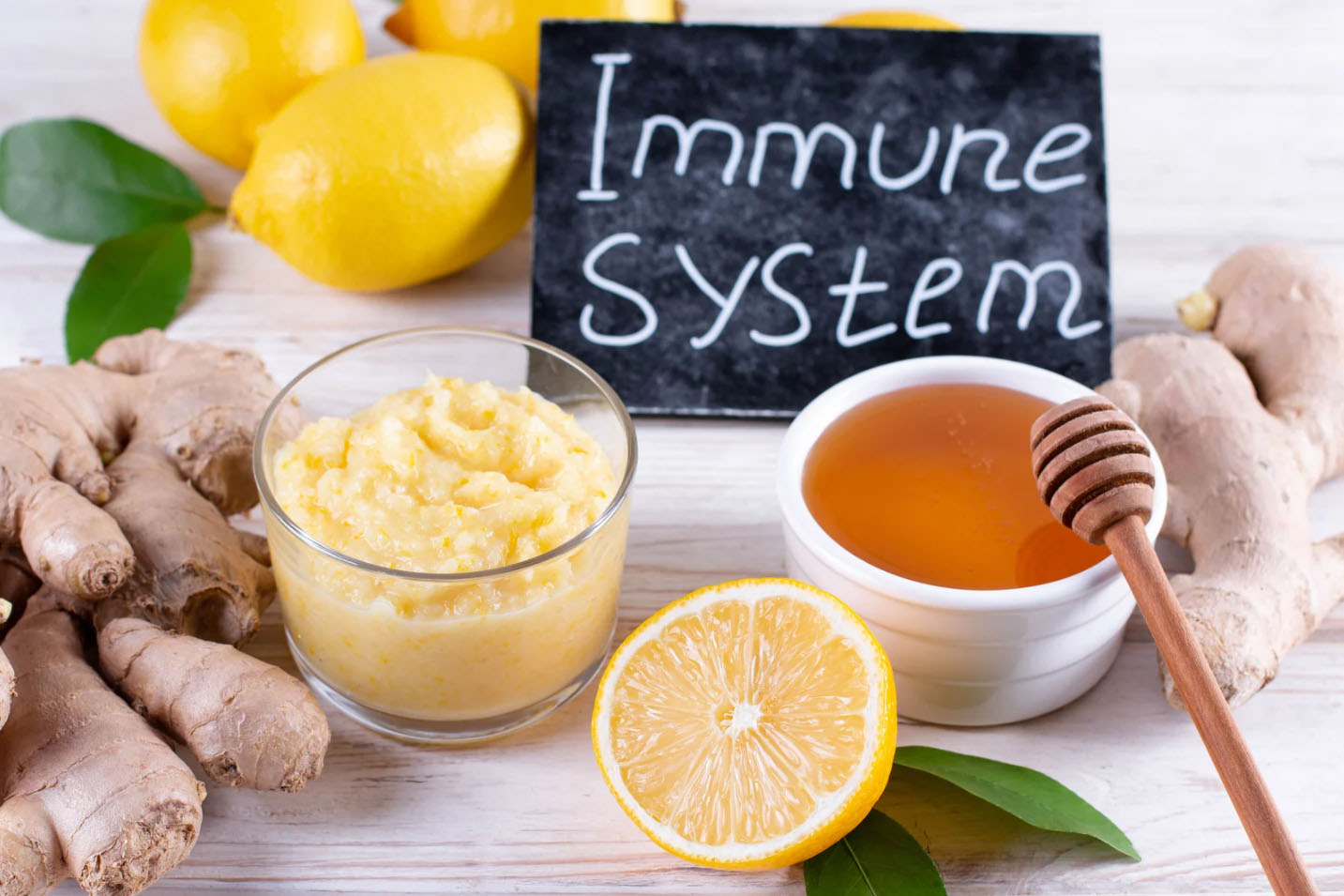 Natural immune-boosting ingredients including ginger, lemons, honey, and a homemade remedy, with a chalkboard sign reading 'Immune System' in the background.