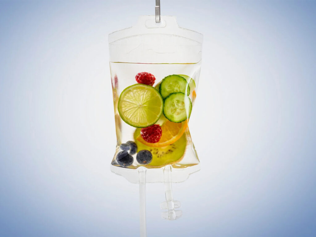 IV drip bag filled with fresh fruits and vegetables, including lime, cucumber, berries, and orange slices, symbolizing hydration and wellness benefits.