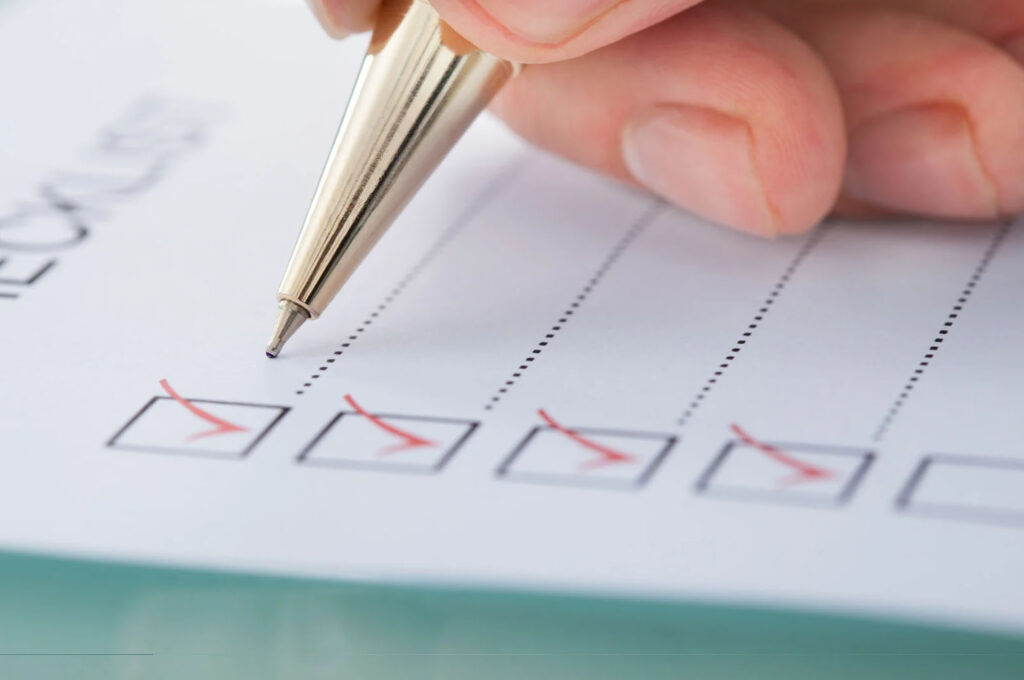 A close-up of a hand holding a pen, ticking off boxes on a printed checklist.