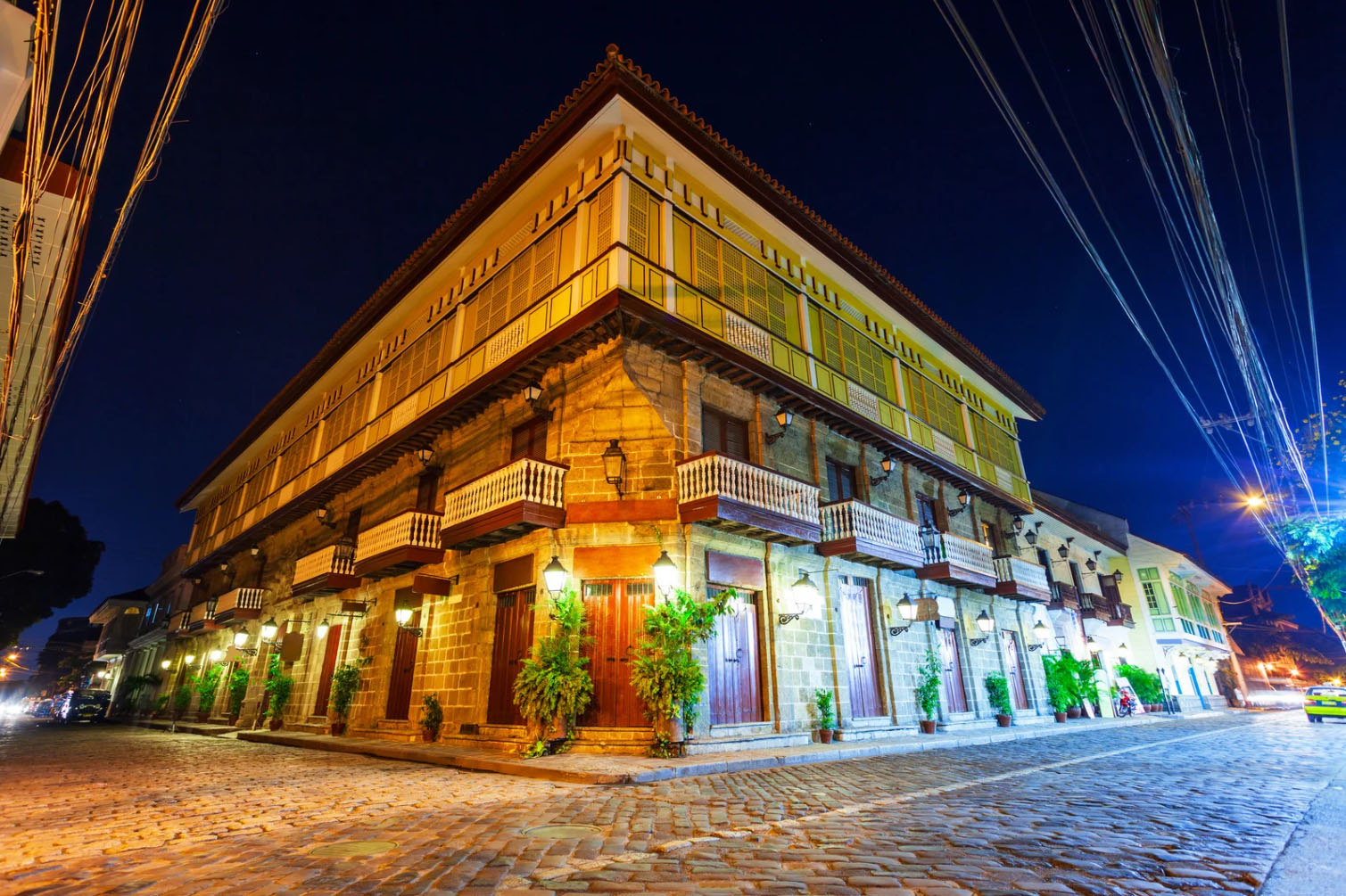 Illuminated Spanish colonial building in Intramuros, Manila at night, showcasing historic stone architecture, wooden balconies, and cobblestone streets.